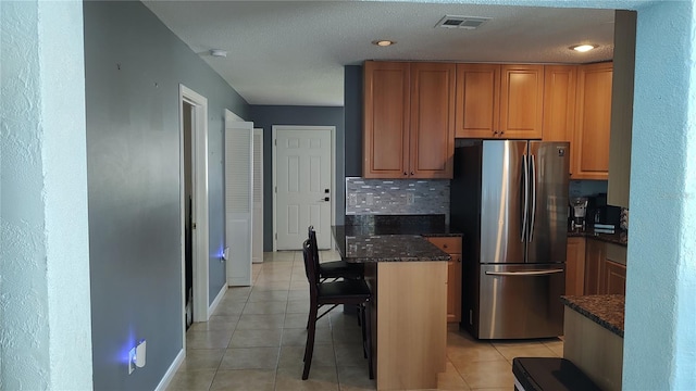 kitchen featuring stainless steel fridge, dark stone countertops, a breakfast bar area, and light tile patterned flooring