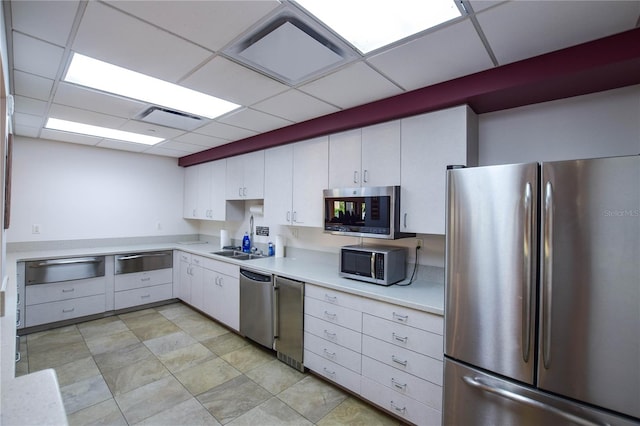 kitchen with white cabinets, a paneled ceiling, sink, appliances with stainless steel finishes, and light tile patterned flooring