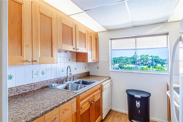 kitchen with white dishwasher, light hardwood / wood-style floors, sink, a drop ceiling, and tasteful backsplash