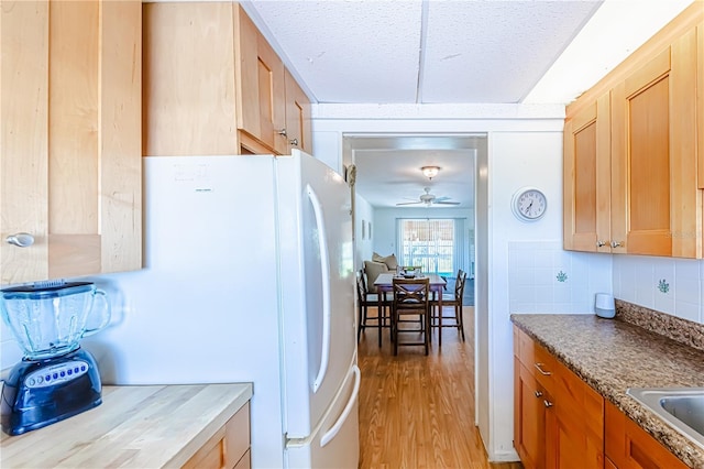 kitchen featuring white fridge, a textured ceiling, light hardwood / wood-style flooring, ceiling fan, and decorative backsplash