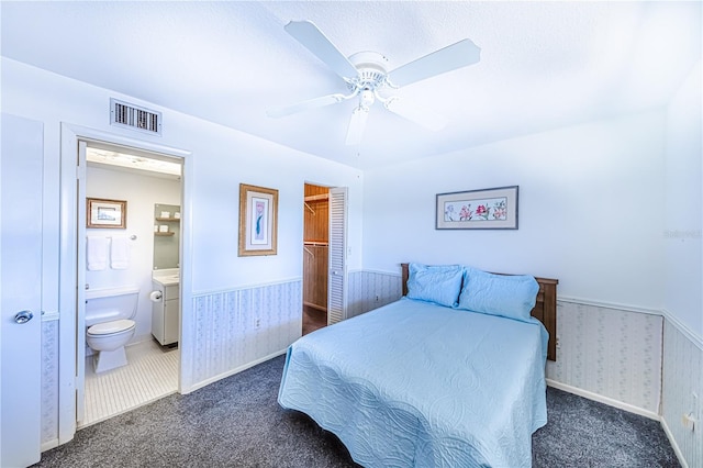 bedroom with ensuite bath, dark carpet, ceiling fan, and a closet