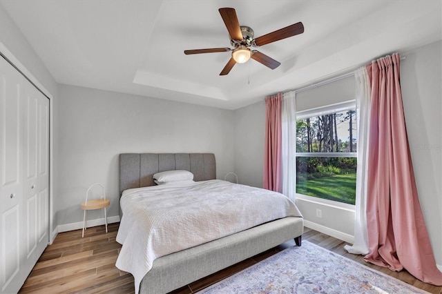 bedroom with a raised ceiling, ceiling fan, a closet, and hardwood / wood-style flooring