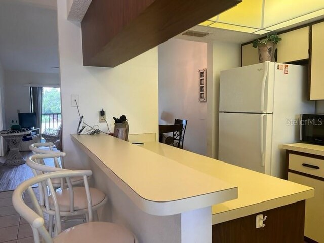 kitchen with white fridge, tile patterned flooring, a breakfast bar, kitchen peninsula, and dark brown cabinetry