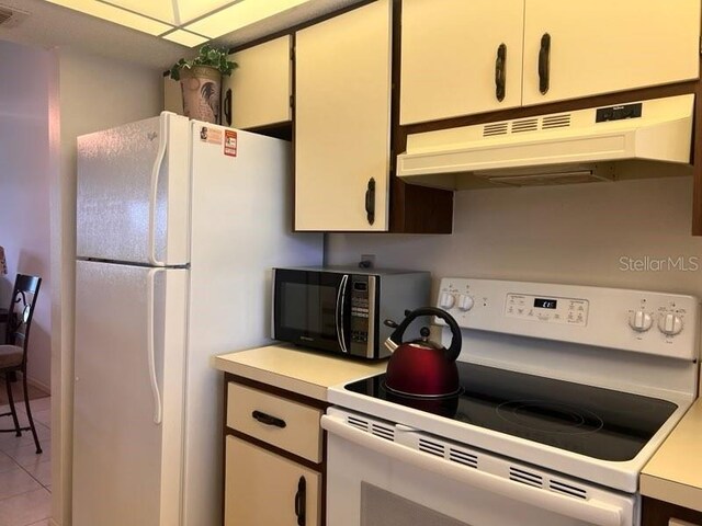 kitchen featuring white appliances, light tile patterned flooring, and white cabinets