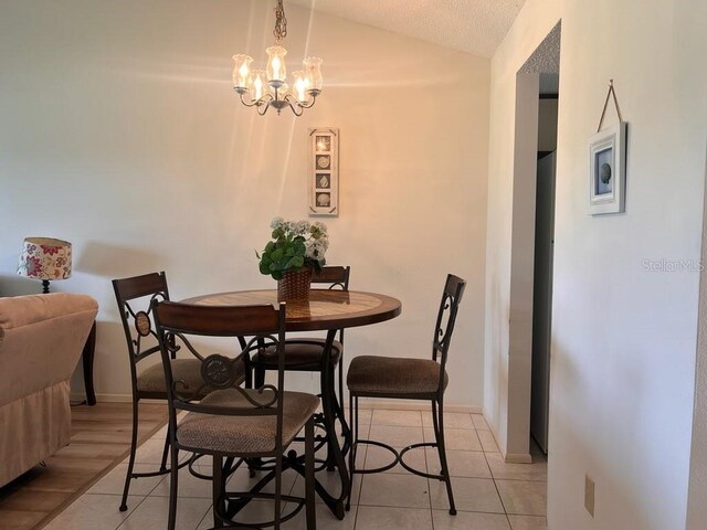 tiled dining room featuring lofted ceiling, a notable chandelier, and a textured ceiling