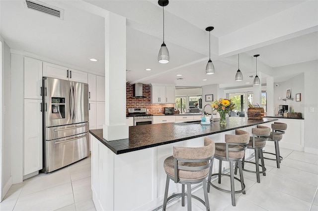 kitchen featuring a spacious island, stainless steel appliances, a kitchen breakfast bar, wall chimney exhaust hood, and white cabinets