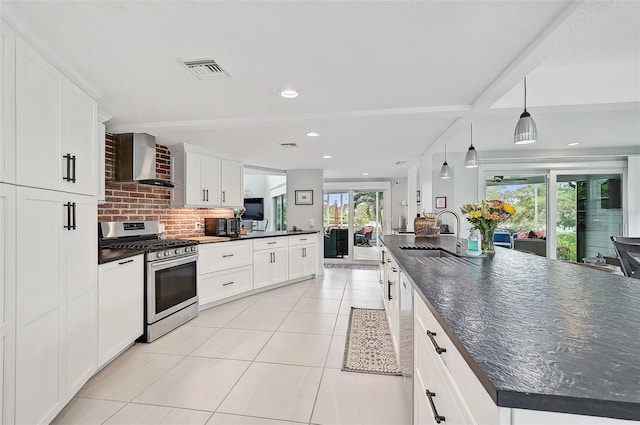 kitchen featuring pendant lighting, stainless steel gas range, decorative backsplash, wall chimney exhaust hood, and a center island with sink