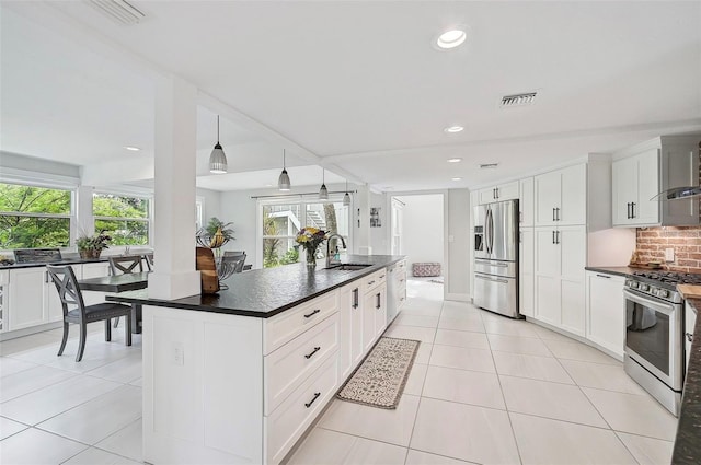 kitchen with white cabinets, stainless steel appliances, sink, an island with sink, and pendant lighting