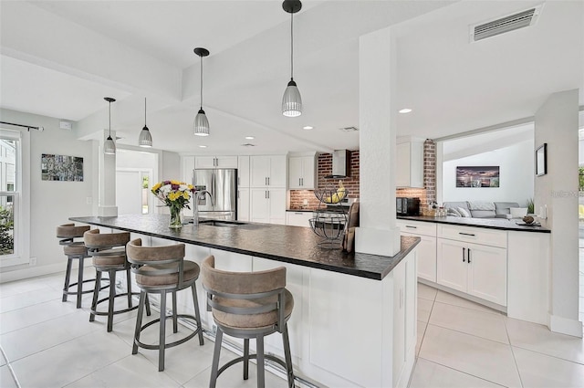 kitchen featuring stainless steel fridge, white cabinetry, a center island with sink, and pendant lighting