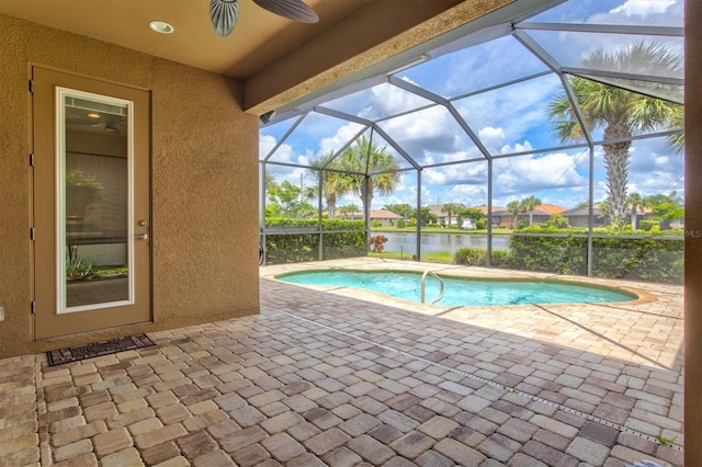 view of pool featuring glass enclosure, ceiling fan, a water view, and a patio