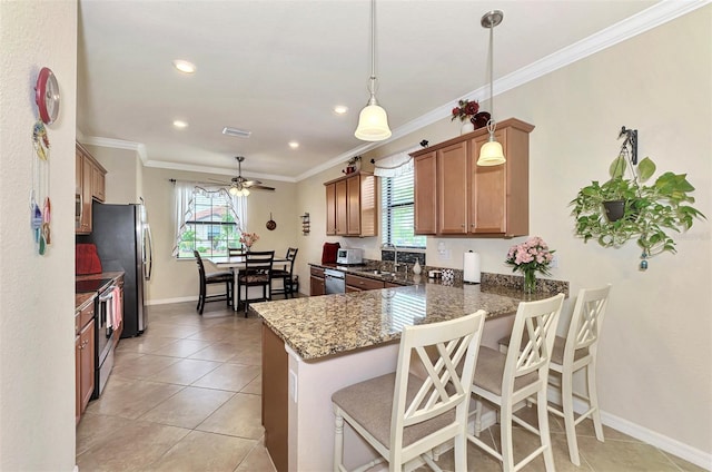 kitchen featuring dark stone counters, a kitchen breakfast bar, ceiling fan, hanging light fixtures, and appliances with stainless steel finishes