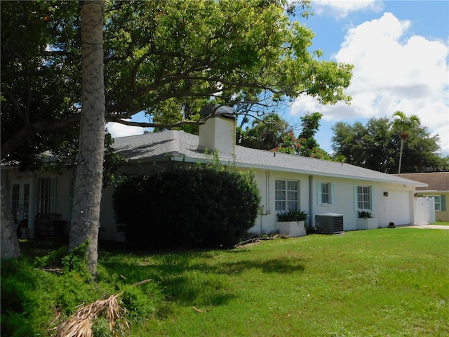 back of house with a garage, cooling unit, a chimney, and a yard