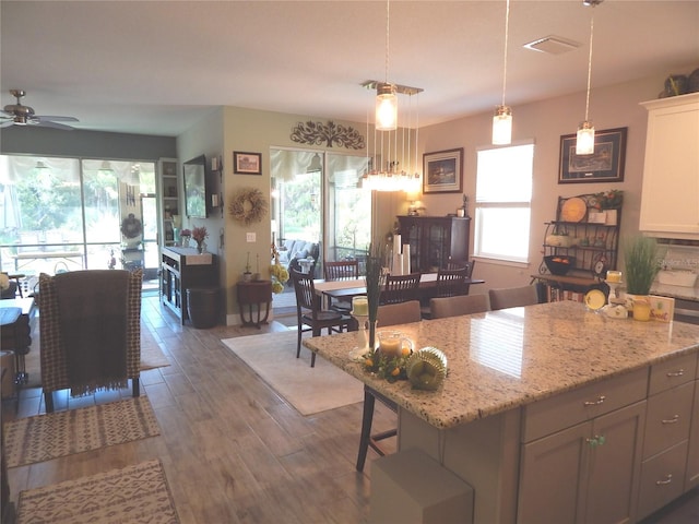 kitchen featuring a kitchen bar, decorative light fixtures, a kitchen island, ceiling fan, and dark wood-type flooring