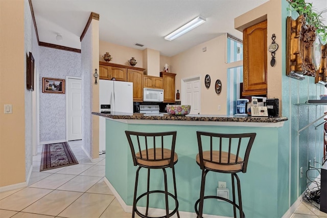 kitchen with dark stone countertops, white appliances, kitchen peninsula, and a breakfast bar