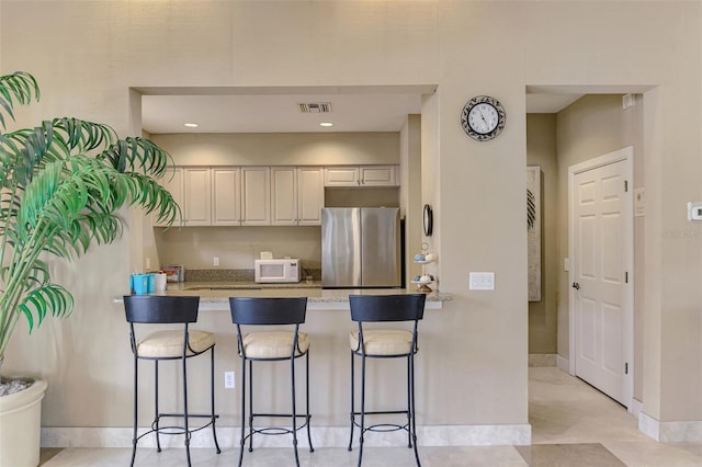 kitchen featuring a kitchen bar, stainless steel fridge, and light stone countertops