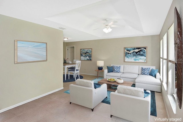 living room featuring a raised ceiling, ceiling fan, and light tile patterned flooring