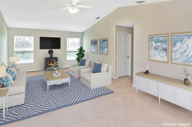 tiled living room with ceiling fan, a wood stove, a wealth of natural light, and vaulted ceiling