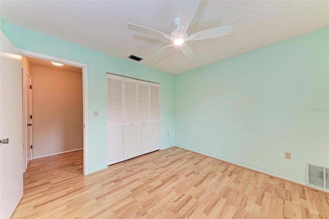 unfurnished bedroom featuring ceiling fan, a closet, a textured ceiling, and light wood-type flooring