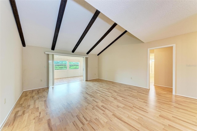 unfurnished living room featuring vaulted ceiling with beams, a textured ceiling, and light wood-type flooring