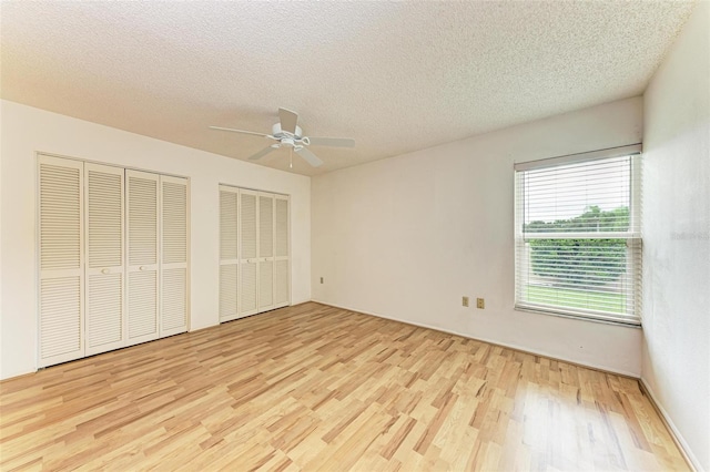 unfurnished bedroom featuring a textured ceiling, light hardwood / wood-style floors, ceiling fan, and multiple closets