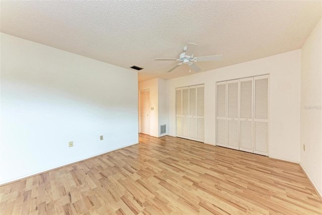 unfurnished bedroom featuring ceiling fan, multiple closets, a textured ceiling, and light hardwood / wood-style flooring