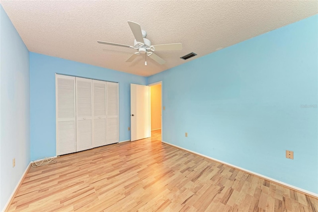 unfurnished bedroom with ceiling fan, light wood-type flooring, a textured ceiling, and a closet