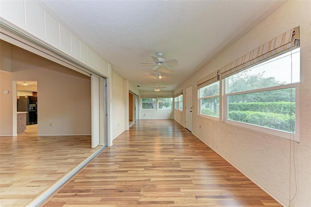 hallway featuring light wood-type flooring, a textured ceiling, and a wealth of natural light