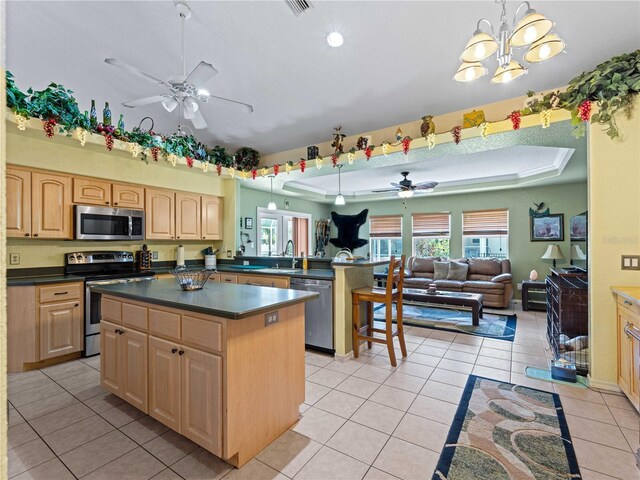 kitchen with ceiling fan with notable chandelier, light tile patterned floors, decorative light fixtures, a tray ceiling, and appliances with stainless steel finishes