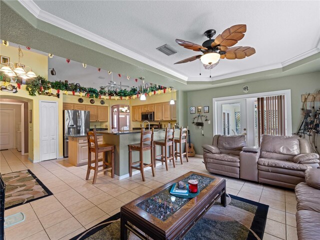 tiled living room with ceiling fan with notable chandelier, a textured ceiling, and a tray ceiling