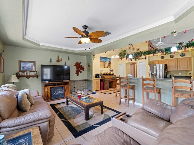 tiled living room featuring a tray ceiling, ceiling fan, and ornamental molding