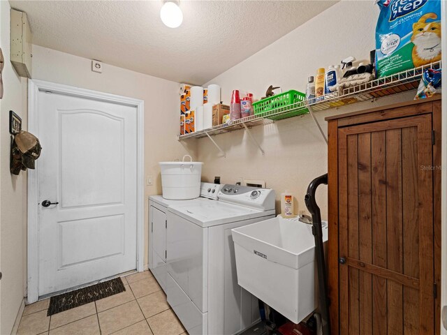 clothes washing area featuring a textured ceiling, washing machine and dryer, light tile patterned floors, and sink