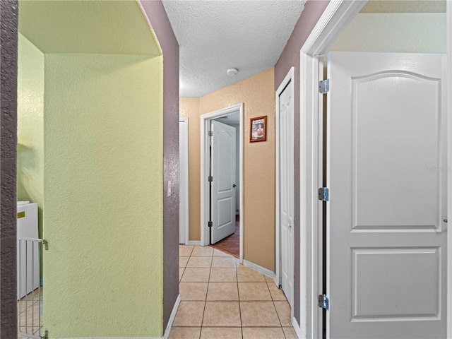 hallway with a textured ceiling and light tile patterned flooring