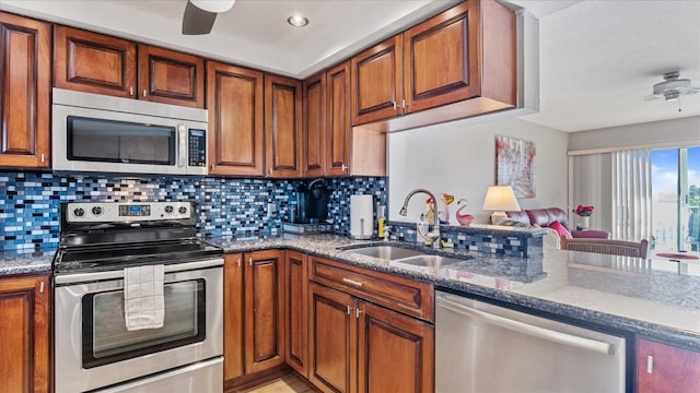 kitchen with brown cabinets, appliances with stainless steel finishes, dark stone counters, and a sink