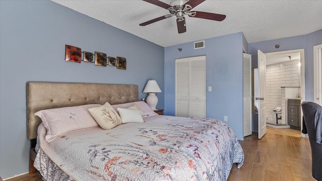 bedroom with ensuite bath, ceiling fan, hardwood / wood-style floors, and a textured ceiling