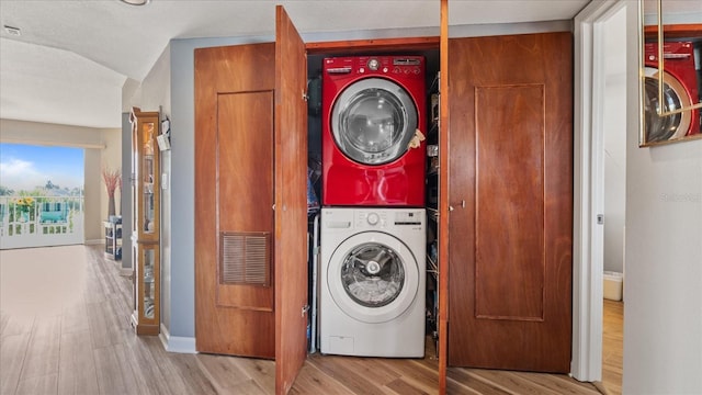 clothes washing area featuring wood finished floors, laundry area, stacked washer / drying machine, baseboards, and visible vents