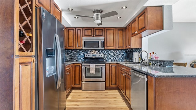 kitchen with a sink, dark stone counters, light wood-type flooring, ceiling fan, and appliances with stainless steel finishes