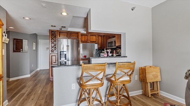 kitchen featuring appliances with stainless steel finishes, a breakfast bar, backsplash, kitchen peninsula, and hardwood / wood-style floors