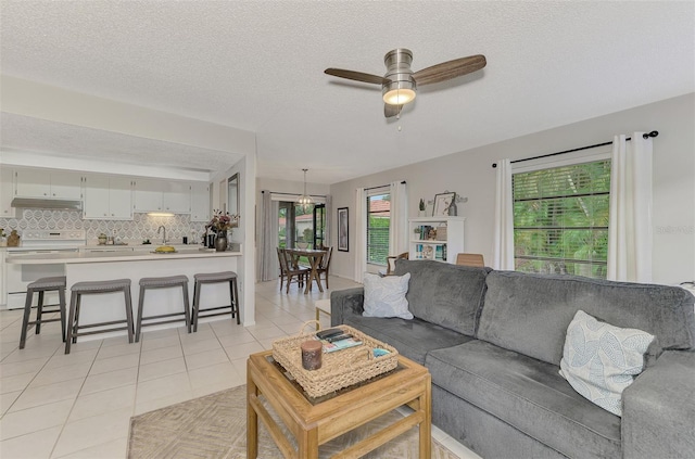 living room with a textured ceiling, ceiling fan, sink, and light tile patterned flooring