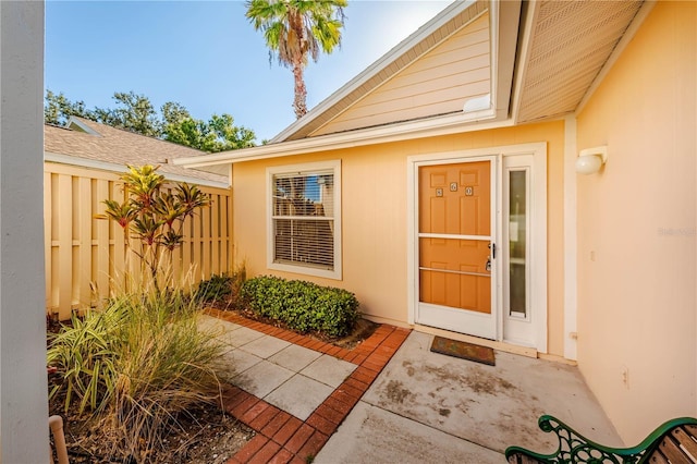 view of exterior entry featuring fence, roof with shingles, and stucco siding