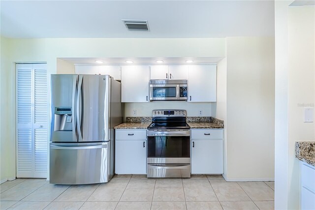 kitchen with dark stone countertops, appliances with stainless steel finishes, white cabinetry, and light tile patterned flooring