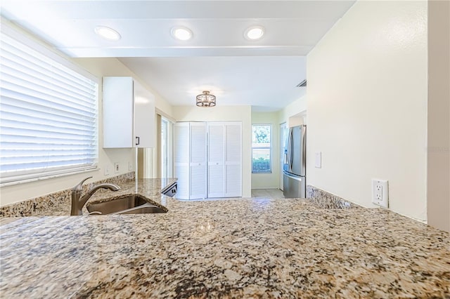 kitchen featuring white cabinets, stainless steel fridge, light stone counters, and sink