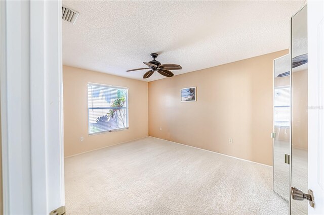 spare room featuring light carpet, a textured ceiling, and ceiling fan