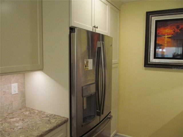 kitchen with white cabinets, stainless steel refrigerator with ice dispenser, tasteful backsplash, and light stone countertops