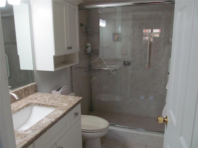 bathroom featuring tile patterned flooring, vanity, a shower with shower door, and toilet