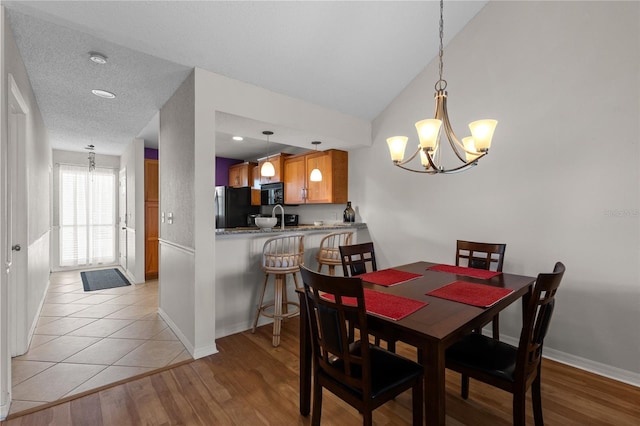 dining room with light hardwood / wood-style floors, vaulted ceiling, a textured ceiling, sink, and a notable chandelier