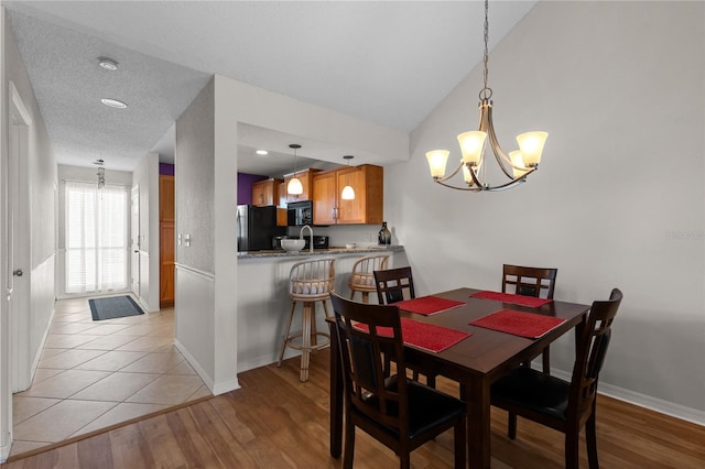 dining space with lofted ceiling, light wood finished floors, a textured ceiling, and baseboards