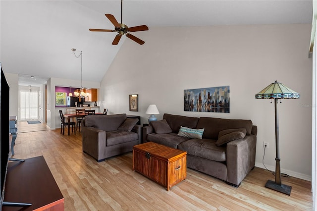 living area with ceiling fan with notable chandelier, high vaulted ceiling, light wood-style flooring, and baseboards