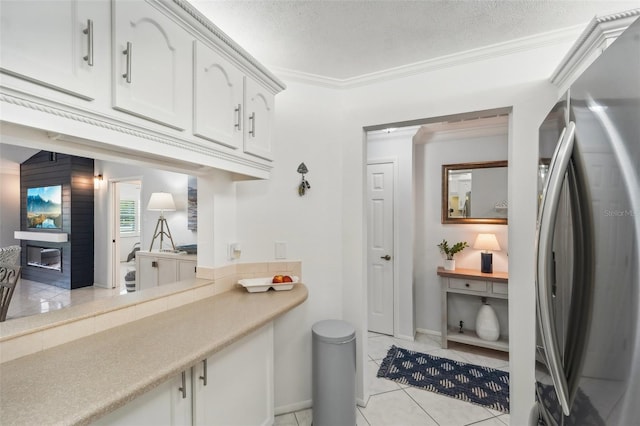 interior space featuring stainless steel refrigerator, white cabinetry, a textured ceiling, light tile patterned floors, and ornamental molding