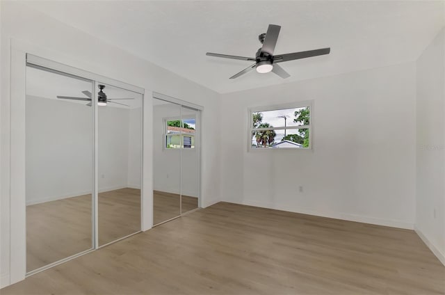 unfurnished bedroom featuring baseboards, a ceiling fan, light wood-style floors, and two closets