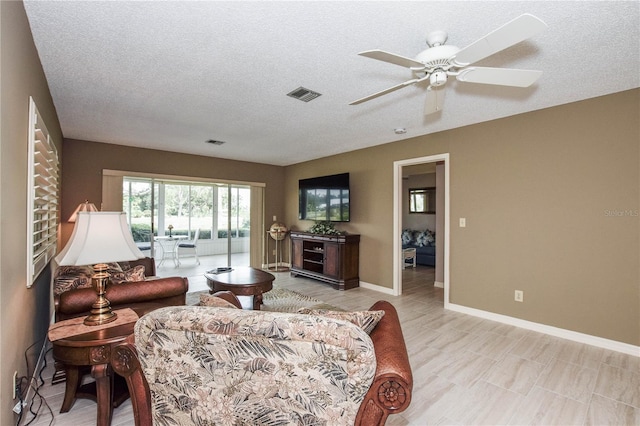 living area featuring visible vents, ceiling fan, a textured ceiling, and baseboards